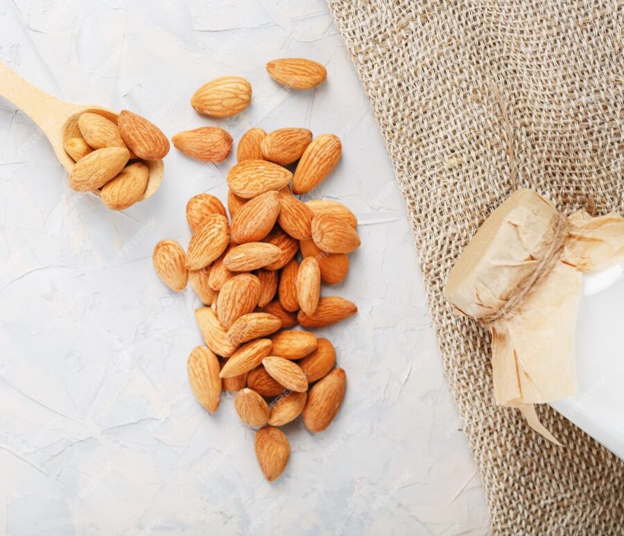 almond-milk-bottle-with-handful-grains-wooden-spoon-with-burlap-cloth-light-background-top-view_94046-8972